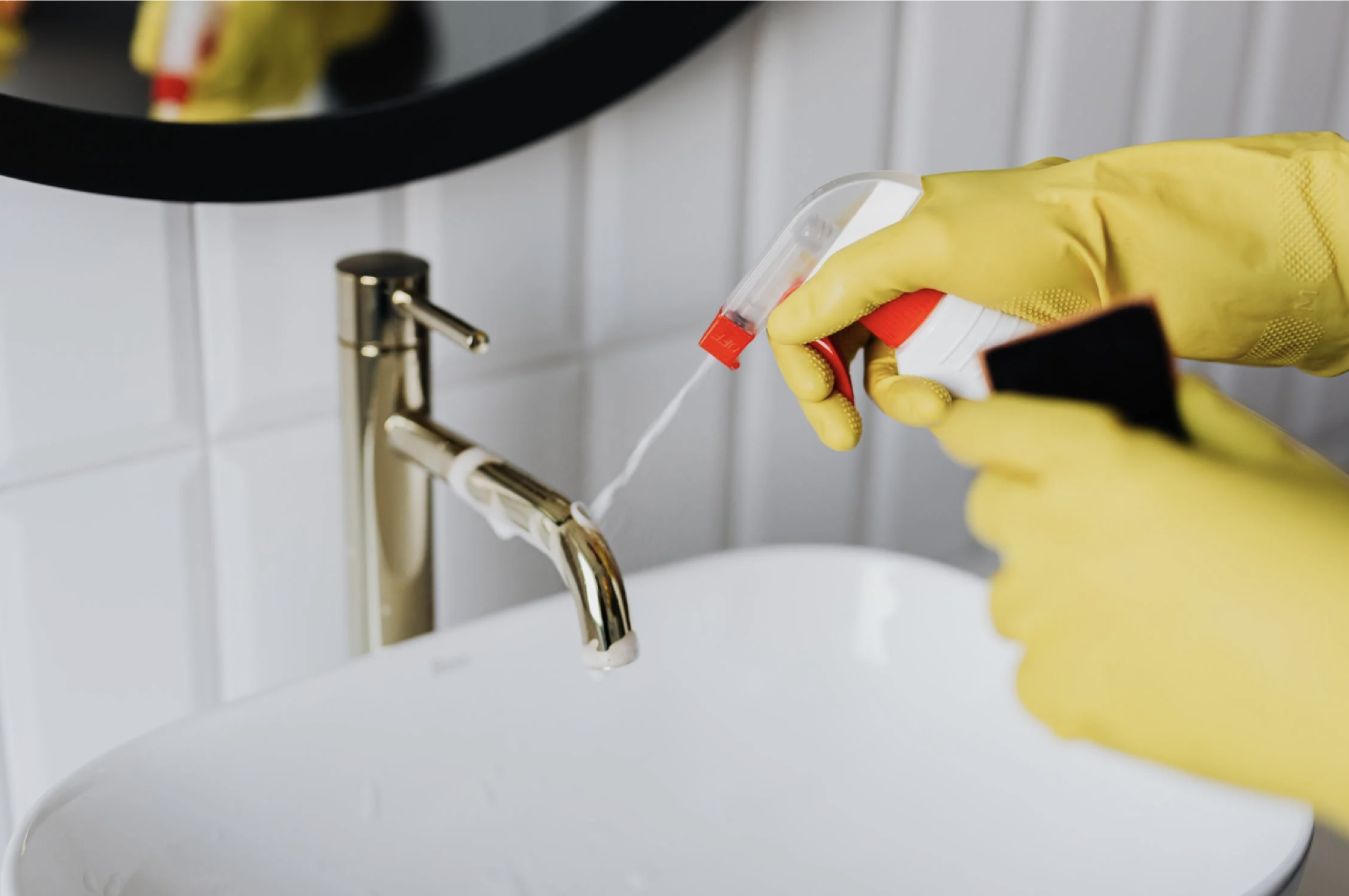 gloved hands spraying cleaner on the spout of a bathroom sink